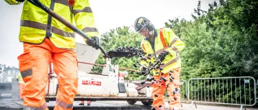 Two Aggregate Industries workers laying asphalt on a road with a shovel