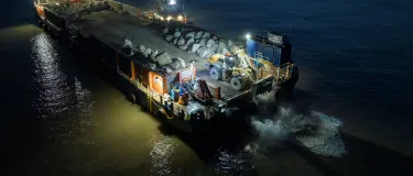 A sea barge at night carries a delivery of Armourstone granite boulders from Glensanda to Blue Anchor Beach, Somerset.