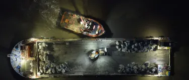 Top down image of the SeaRock barge being moved into position by a tug boat at night