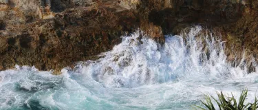 Top down view of the coast with waves splashing against a rocky cliff