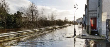 Road submerged by floodwater with a person walking along the path