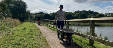 A volunteer from Aggregate Industries pushes a wheelbarrow as part of activity taking place at Codnor Park Reservoir in Derbyshire