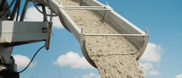 Close-up of wet ready-mix concrete pouring from a mixer truck chute onto a construction foundation.
