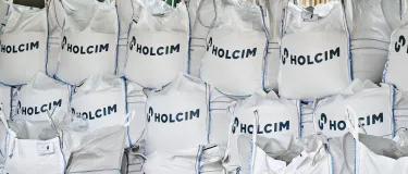 Stack of large heavy duty sacks containing aggregate with the Holcim logo on each bag