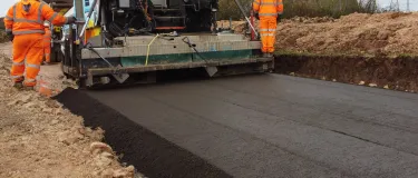paving asphalt in front of a power station cooling tower with workers