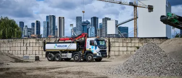 Truck with Holcim branding in a yard with piles of aggregates and the london skyline behind