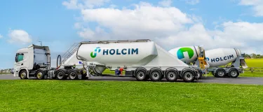 Holcim branded trucks and mixers lined up on a road in an open field