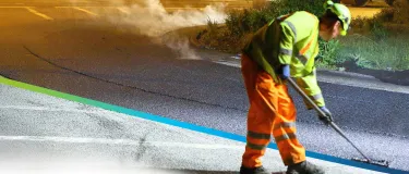 Worker in PPE pushing fresh asphalt into place on a road