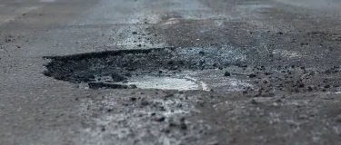 Road with a car driving in the background and a pothole in the foreground