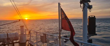 Sunset over the sea with a flag in the for-ground on a large ship