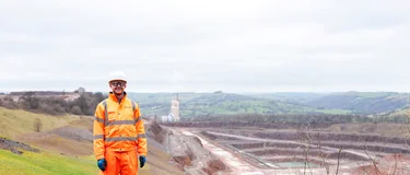 Head of Sustainability for HOlcim UK, Tom Redfern in high viz PPE with Cauldon Quarry and cement plant in the background