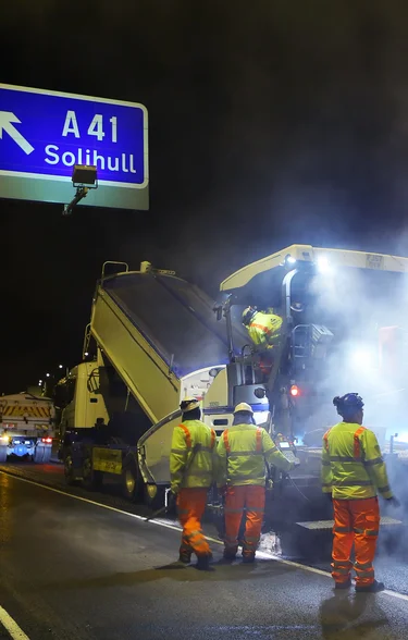 Workers in high viz clorthing follow a paver and a truck as it resurfaces part of the M42 motorwat junction 6.