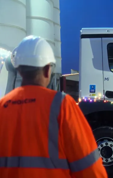 Mixer truck with christmas lights around it at night with a man in PPE in the foreground