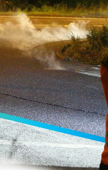 Worker in PPE pushing fresh asphalt into place on a road