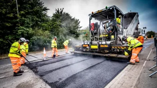 Aggregate Industries workers resurfacing a road with tools and machinery.