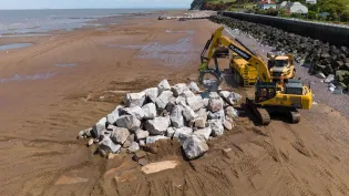 A pile of Armourstone granite boulders on Blue Anchor beach Somerset with a digger. It is part of coastal defence work.