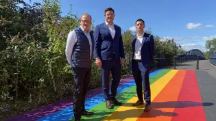 Hr Director James Roberts, Surfacing Solutions Managing Director Tom Edgcumbe and High Viz LGBTQ+ Network Lead Aron Simpson-Webb stand on a new Pride themed pathway on the way into Leicester Pride at Abbey Park