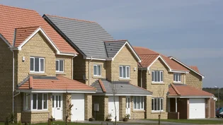Row of modern brick and render houses with manicured lawns and paved driveways at a Dunelm Castle Homes development.