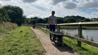 A volunteer from Aggregate Industries pushes a wheelbarrow as part of activity taking place at Codnor Park Reservoir in Derbyshire
