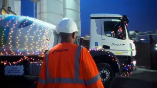 Mixer truck with christmas lights around it at night with a man in PPE in the foreground