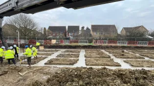 open area with workmen in PPE pouring concrete into a foundation area