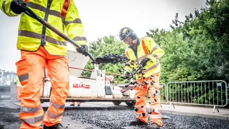 Worker shovels fresh asphalt onto new road