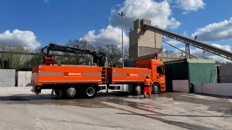An orange Besblock lorry being loaded with blocks in a yard.