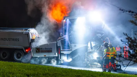 Aggregate Industries truck tipping asphalt into a paver at night with steam
