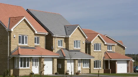 Row of modern brick and render houses with manicured lawns and paved driveways at a Dunelm Castle Homes development.