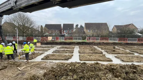 open area with workmen in PPE pouring concrete into a foundation area