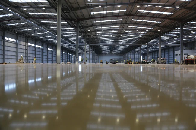 Newly constructed empty warehouse featuring a freshly laid, wet self-leveling floor screed.