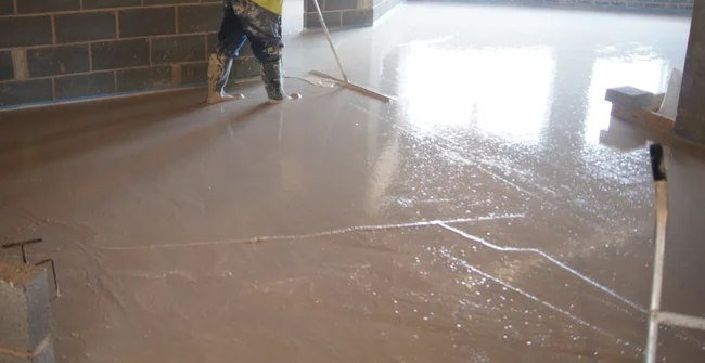 A construction worker wearing high-visibility gear installing self-leveling Highflow screed on a floor at Beaumont Hall.