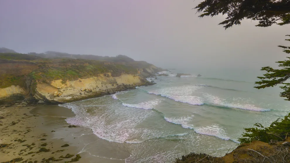Coastal bay with waves crashing onto a sandy beach in an overcast environment