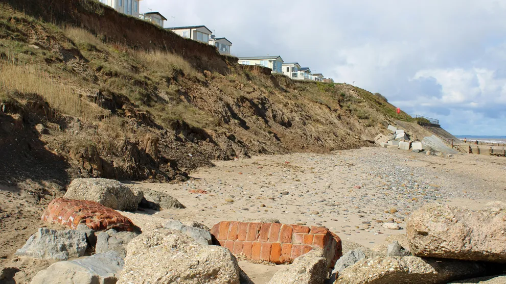 Small houses along a cliff edge, leading to a rocky beach at the sea