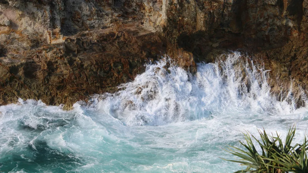 Top down view of the coast with waves splashing against a rocky cliff