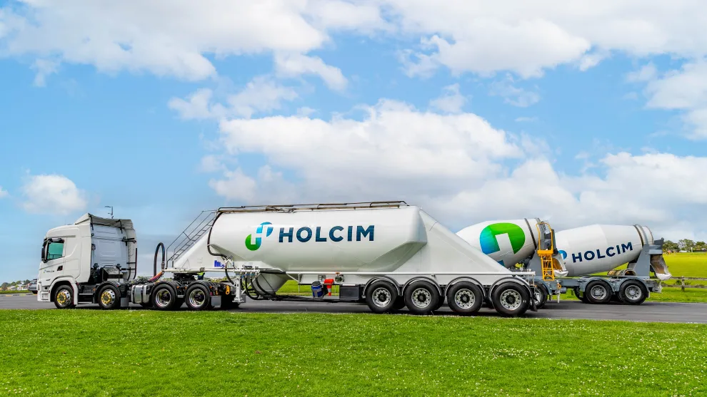 Holcim branded trucks and mixers lined up on a road in an open field