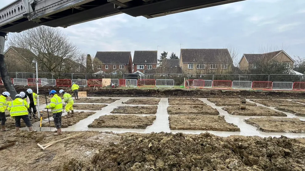 open area with workmen in PPE pouring concrete into a foundation area