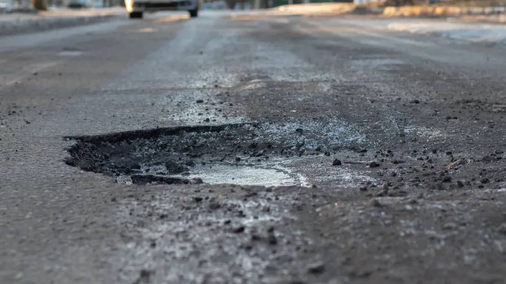 Road with a car driving in the background and a pothole in the foreground