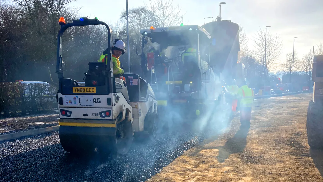Roller going over fresh asphalt with steam and light rays