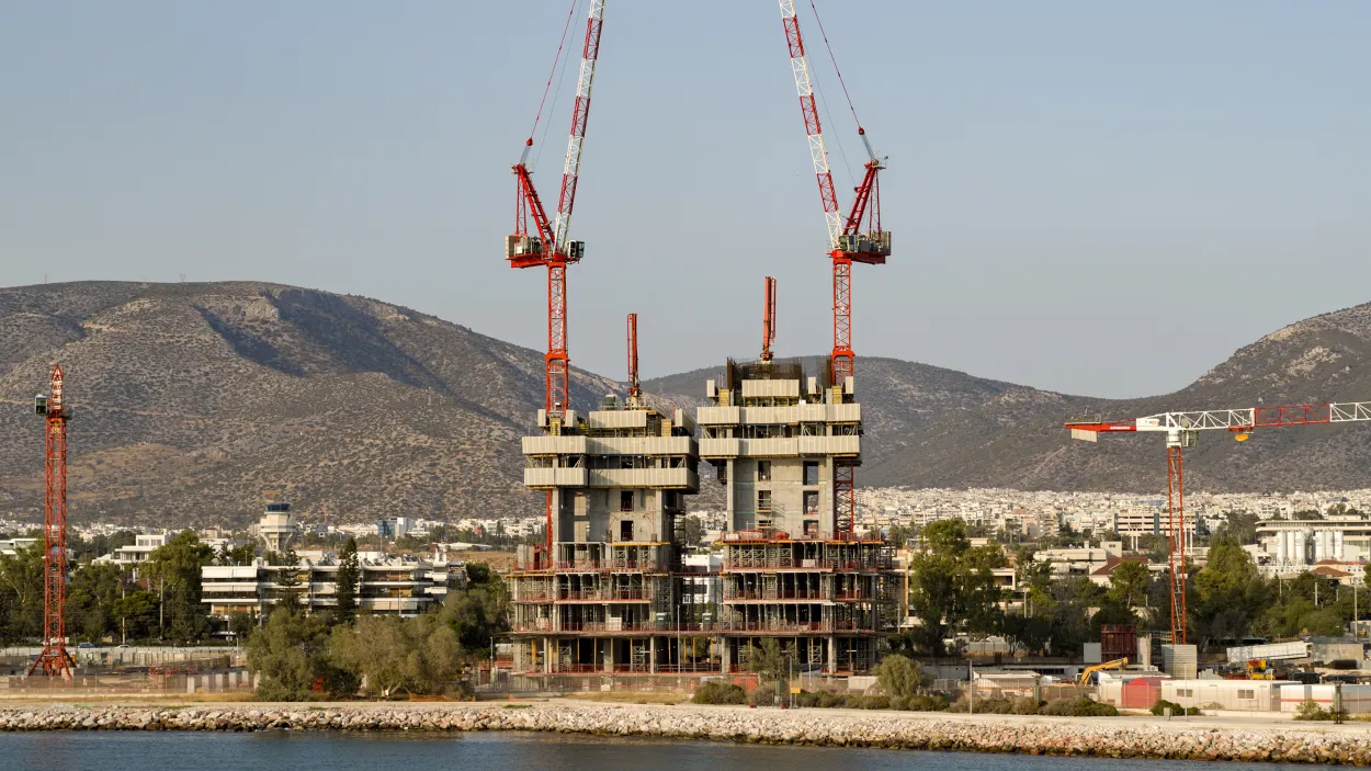 Tower under construction with two cranes and a city skyline