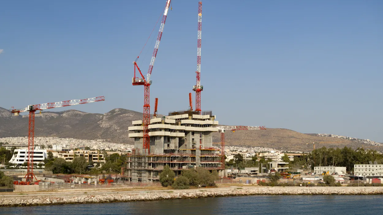 Tower under construction with three cranes and a city skyline