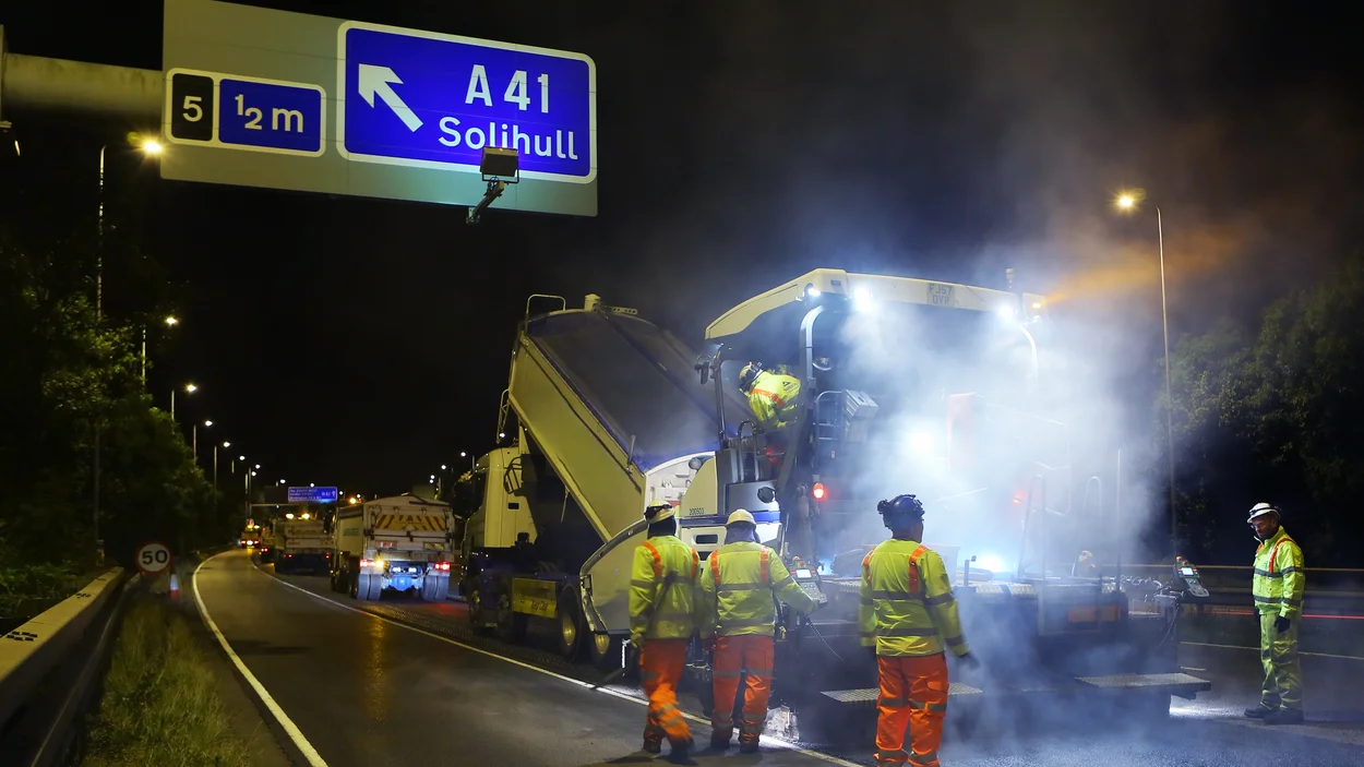 Workers in high viz clorthing follow a paver and a truck as it resurfaces part of the M42 motorwat junction 6.