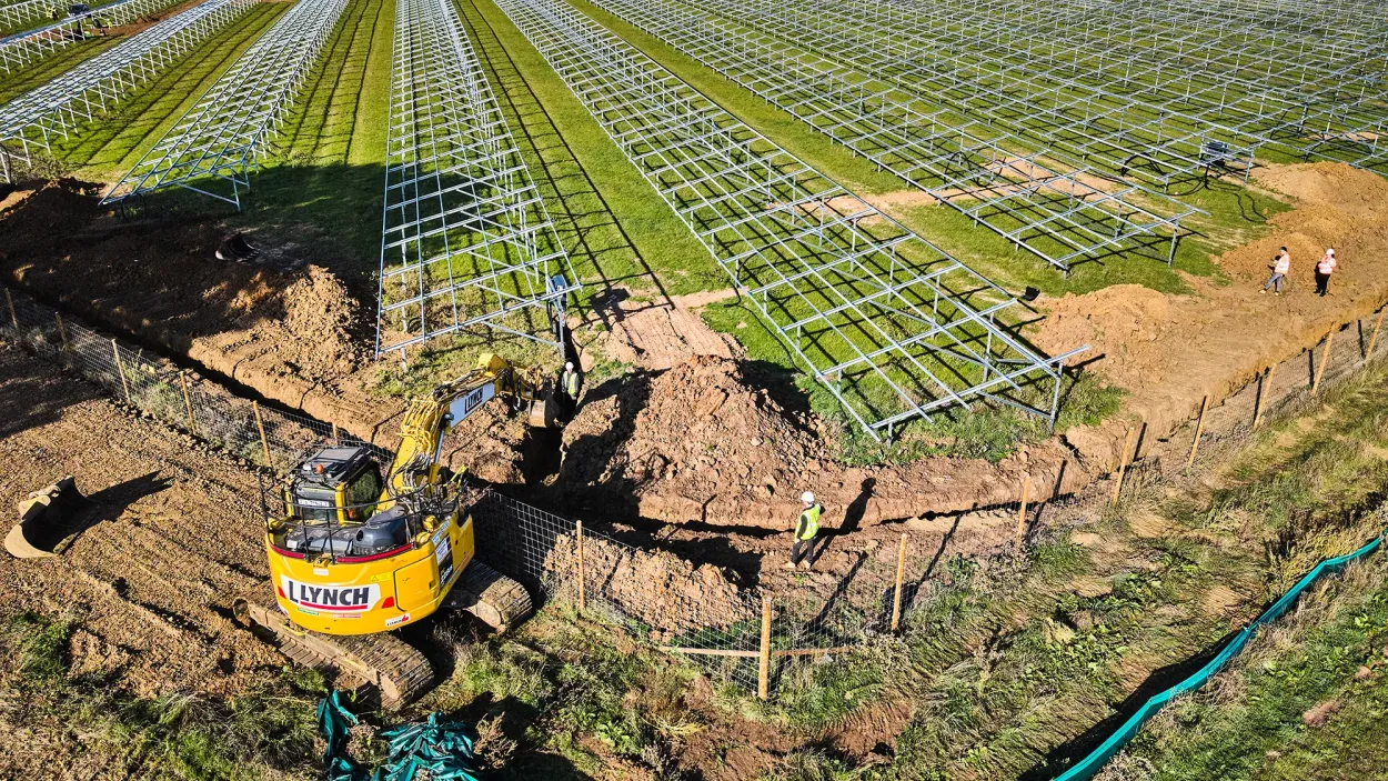 drone image of an excavator digging soil next to rows of solar panel frames