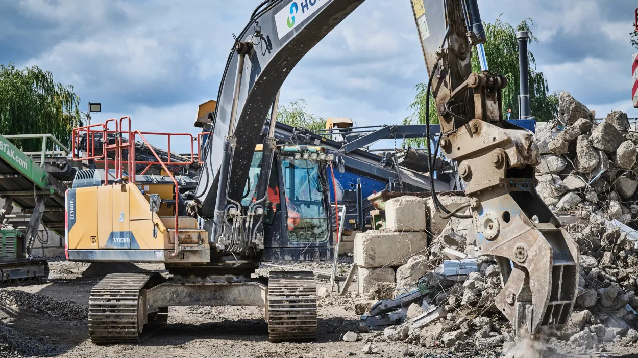 Excavator with Holcim branding crushing construction demolition material