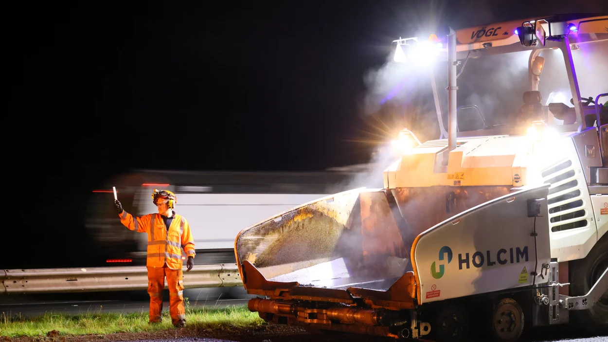 A work in high vis stands near a Holcim paver as it operates on the M5 motorway