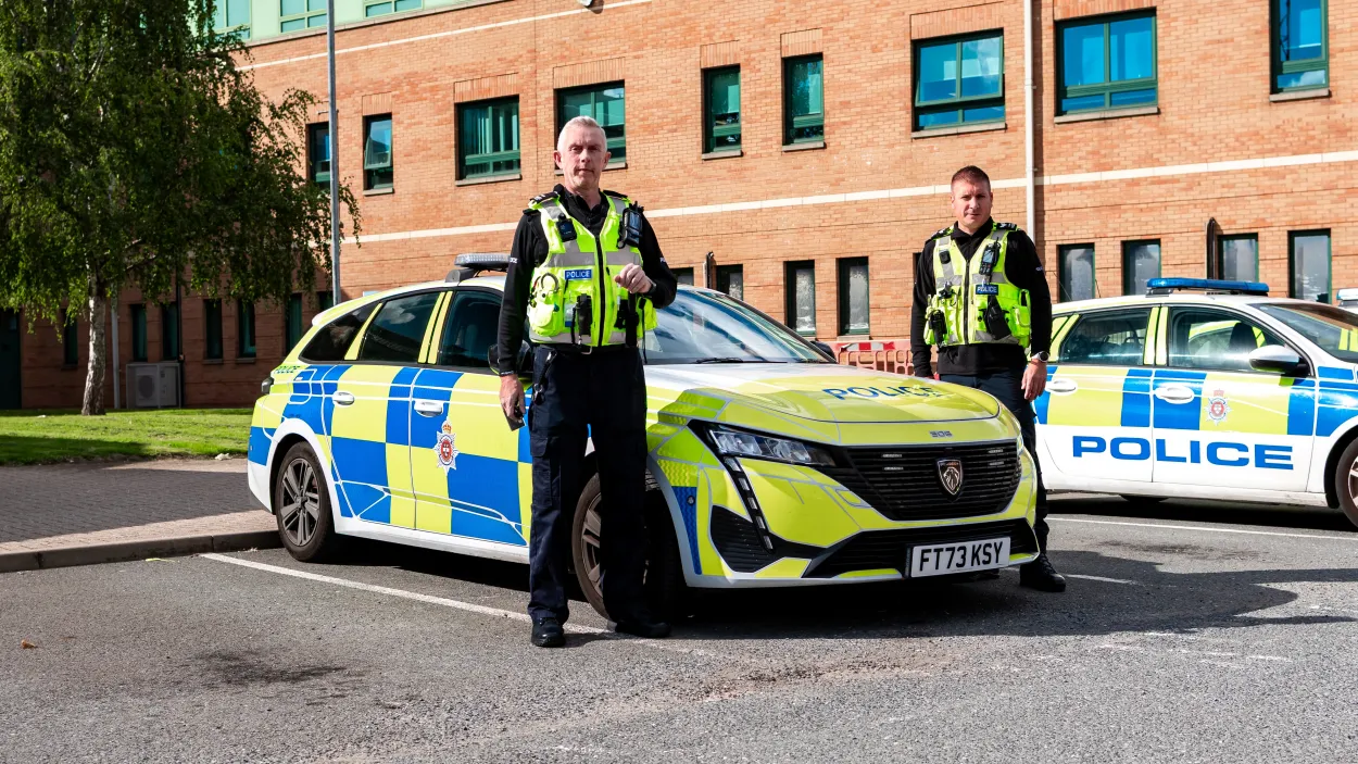 Rob Walsh stood next to a police car and a colleague at St Mary's Wharf police station in Derby