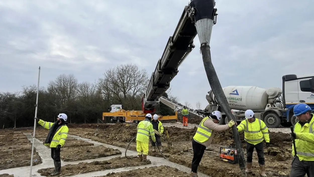 Workers in PPE pouring concrete into the foundations of a housing development in Thornwood