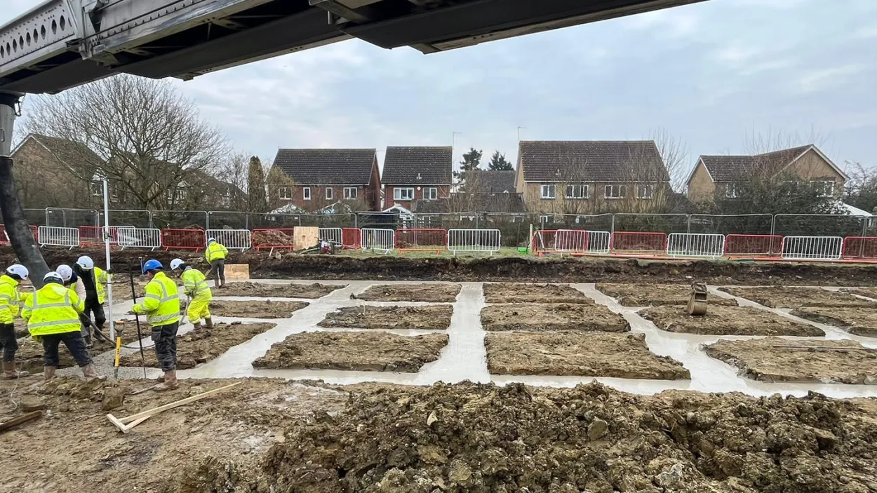open area with workmen in PPE pouring concrete into a foundation area