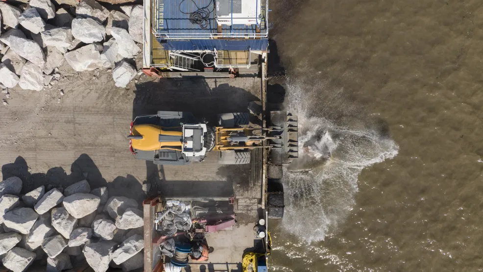 Top down image of heavy load digger dropping Armourstone boulders onto the Blue Anchor Coastline from a barge