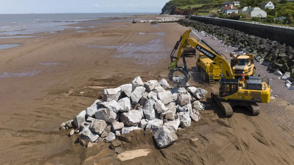 Excavator moving Armourstone granite boulders into position on the Blue Anchor beach